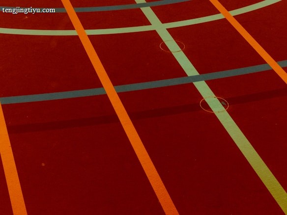 A sports court with intersecting lines in orange and blue, creating geometric patterns on a reddish-brown surface.