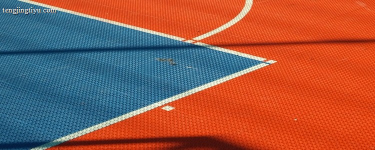 A vibrant sports court with sections of red and blue, featuring crisp white lines marking the boundaries. Shadows from a structure create geometric patterns across the surface, adding depth and interest to the scene.